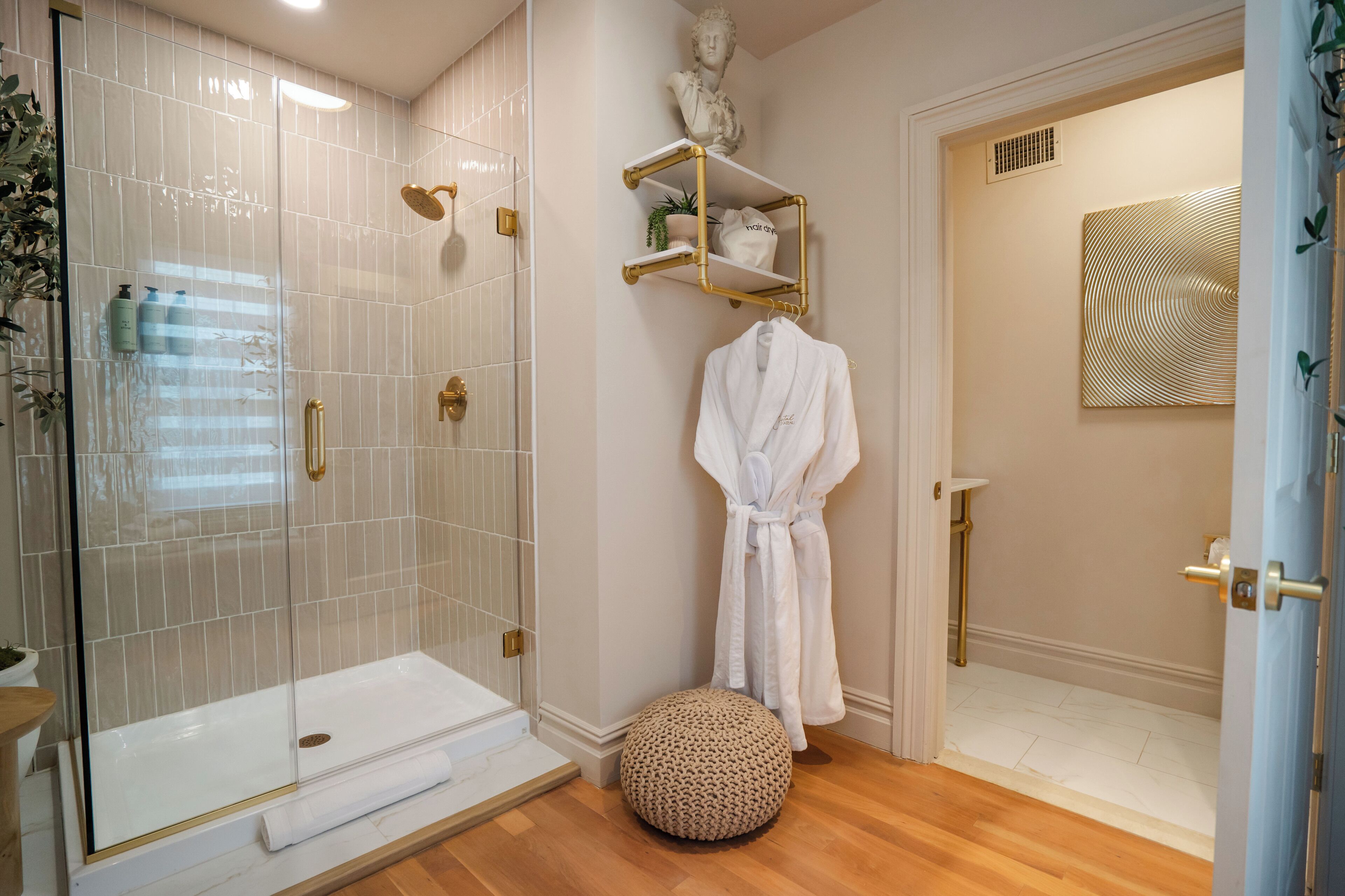 A modern bathroom with a glass-enclosed shower, a white bathtub, and a round ottoman.