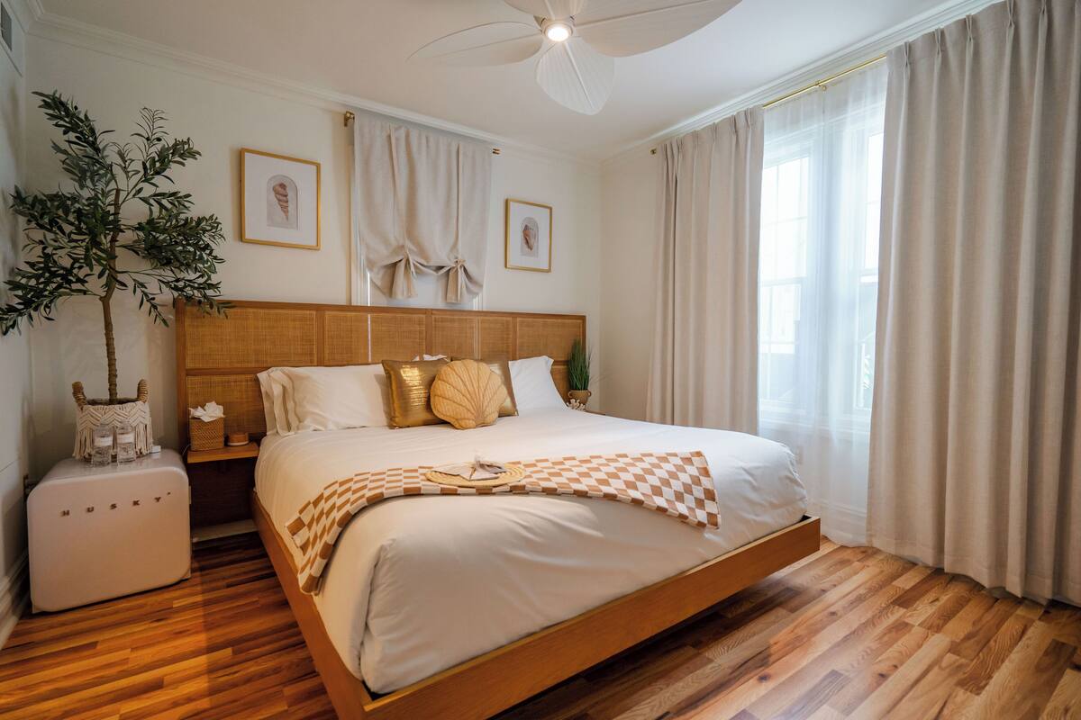 A spacious bedroom with a wooden bed, a ceiling fan, a nightstand, and a potted plant.