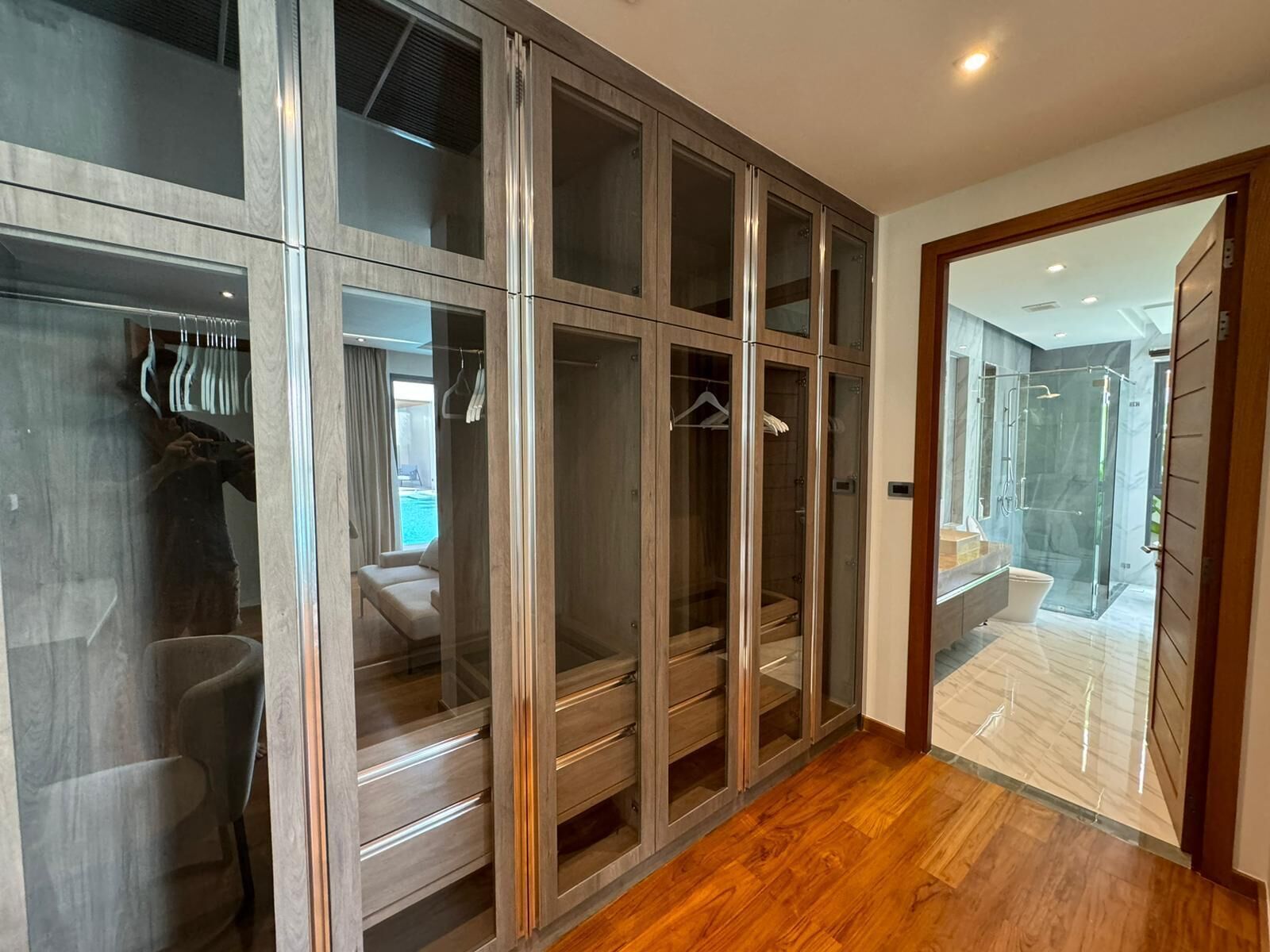 A walk-in closet with mirrored doors and drawers, a wooden floor, and a view of a pool and outdoor area.