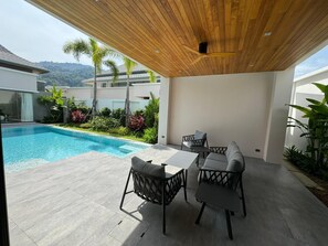 Un patio exterior moderno con piscina, techo de madera y mobiliario exterior.