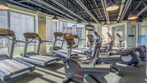 A gym with multiple treadmills and elliptical machines, large windows, and a high ceiling with exposed beams. - Nautical Nest at Laketown Wharf 1019 | Beach Access, Gym, Parking Onsite, 5 Pools (Panama City Beach)