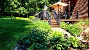 Une cabane en bois dotée d’un balcon, entourée d’une végétation luxuriante et d’une pelouse bien entretenue.