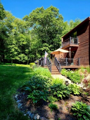Une cabane en bois dotée d’un balcon, entourée d’une végétation luxuriante et d’une pelouse bien entretenue.