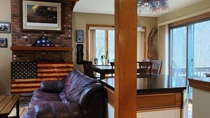 Un vaste espace de vie comprenant un canapé en cuir, un plancher en bois, un mur décoratif en briques et un escalier menant à l’étage supérieur.