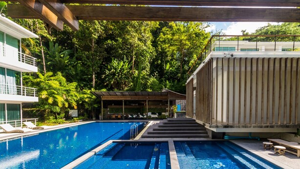 A swimming pool with a wooden deck and lounge chairs, surrounded by lush greenery and a covered seating area. - Private studio at Zen Space by Lofty (Kamala)