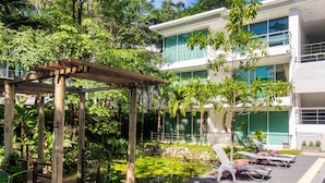 A modern building with a pool area, wooden pergola, and lounge chairs. - Private studio at Zen Space by Lofty (Kamala)
