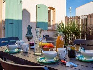 Guests can dine al fresco at this outdoor table set with a pitcher, cups, and a fruit basket.