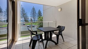 Un balcon avec une table et des chaises, une vue sur les arbres et un parking.