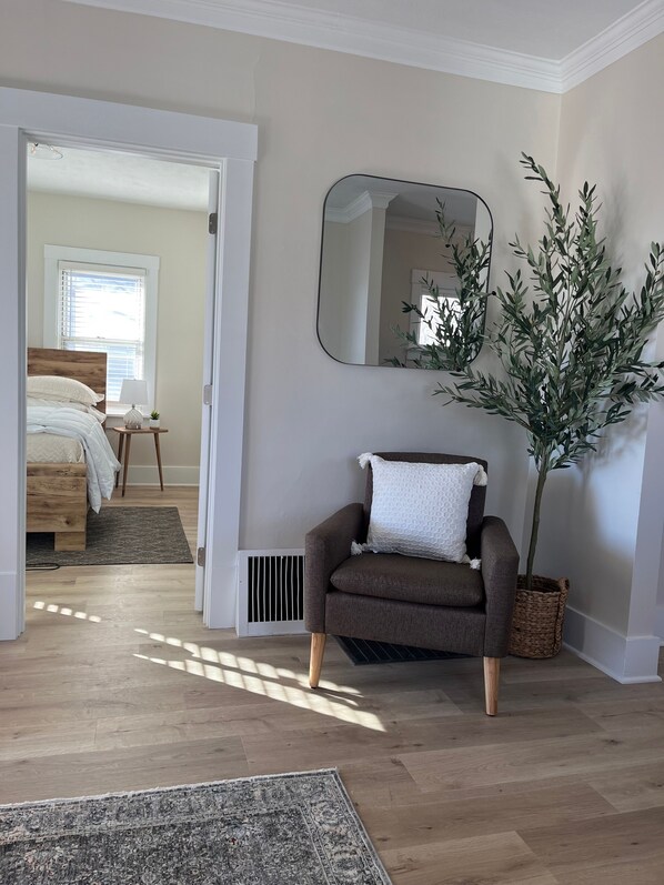 Un dormitorio con cama de madera, una mesita de noche con lámpara, una planta en maceta y un espejo en la pared.