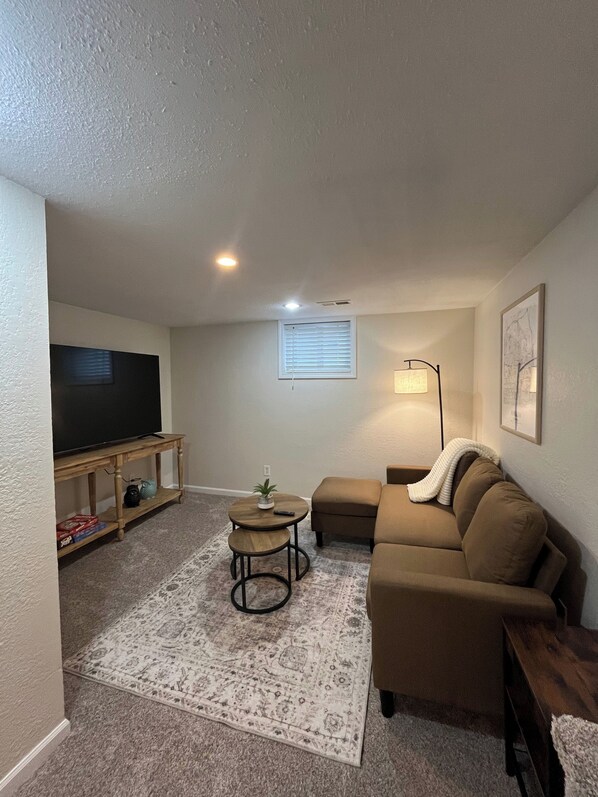 A living room with a flat-screen TV, a sofa, a coffee table, and a patterned rug.