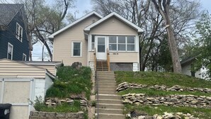 A two-story house with a stone retaining wall and a wooden staircase leading to the front door.
