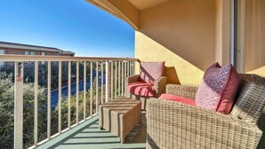 A balcony with wicker furniture, a view of a road, and a building in the background. - Private Beach Access! Free Activities Fun Pass! Ciboney 4013! (Miramar Beach)