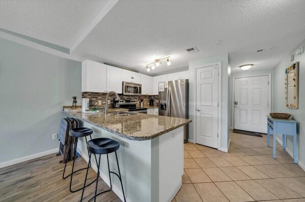 A modern kitchen with a central island, bar stools, a microwave, and a refrigerator. - Private Beach Access! Free Activities Fun Pass! Ciboney 4013! (Miramar Beach)