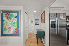 A kitchen with a stainless steel refrigerator, a teal table, and a colorful abstract painting on the wall.