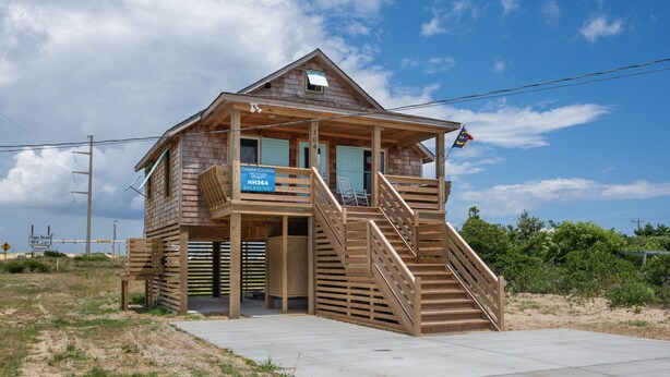 A wooden beach house with a balcony, a staircase, and a sign indicating it is part of the Coastal Carolina NH364. - Nags Head 364: Pet Friendly, Newly Remodeled, Oceanside, Short Stays Anytime! (Nags Head)