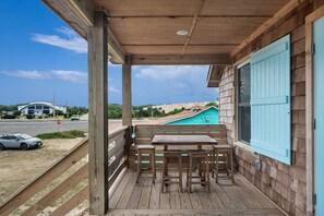 Une terrasse en bois avec une table et des chaises, d’où l’on a vue sur une plage et un bâtiment situé au loin.