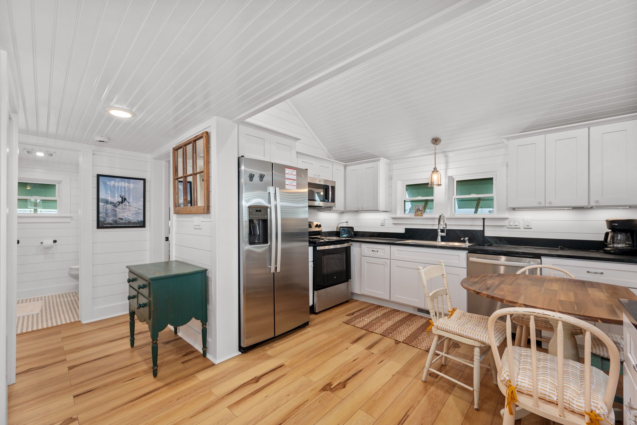 A modern kitchen with white cabinetry, stainless steel appliances, and a wooden dining table.