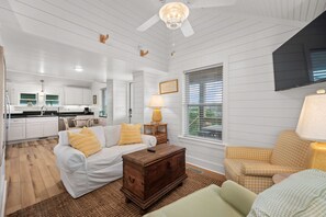 Un salon avec un canapé blanc, une table basse en bois et un fauteuil à motif pied-de-poule.