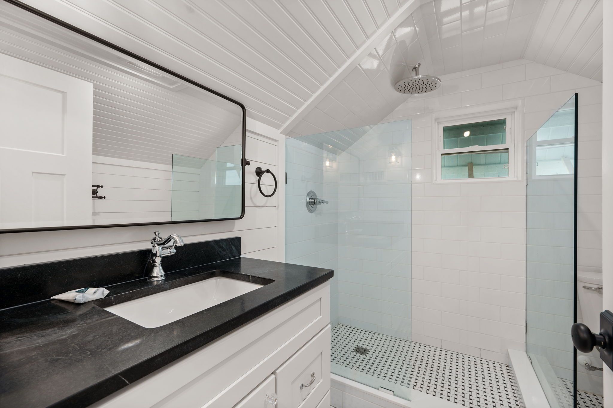 Un baño moderno con un espejo grande, una encimera negra, un lavabo blanco y una zona de ducha con mampara de cristal.