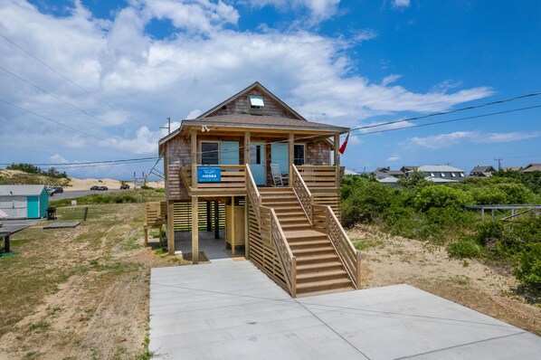 A wooden beach house with a porch, a staircase, and a sign advertising Coastal Carolina Vacations.