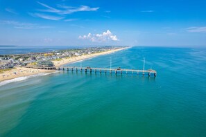 A coastal town with a pier extending into the sea, a beach with umbrellas, and a clear sky.