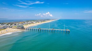 An aerial view of a beach with a long pier extending into the ocean, surrounded by buildings and a clear sky. - Nags Head 364: Pet Friendly, Newly Remodeled, Oceanside, Short Stays Anytime! (Nags Head)