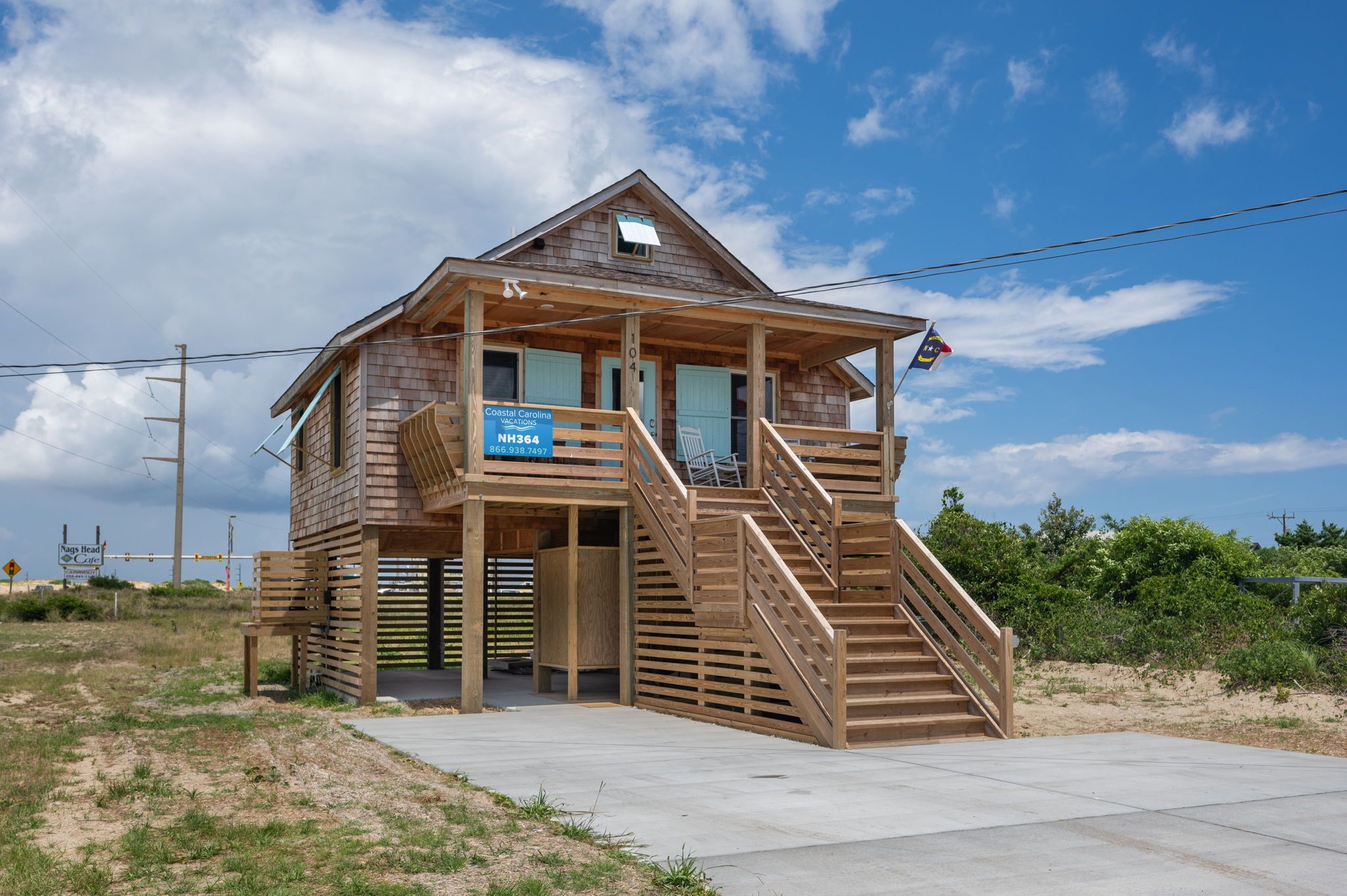 Una casa de playa de madera con un porche, una escalera y un letrero de Coastal Carolina Vacations.