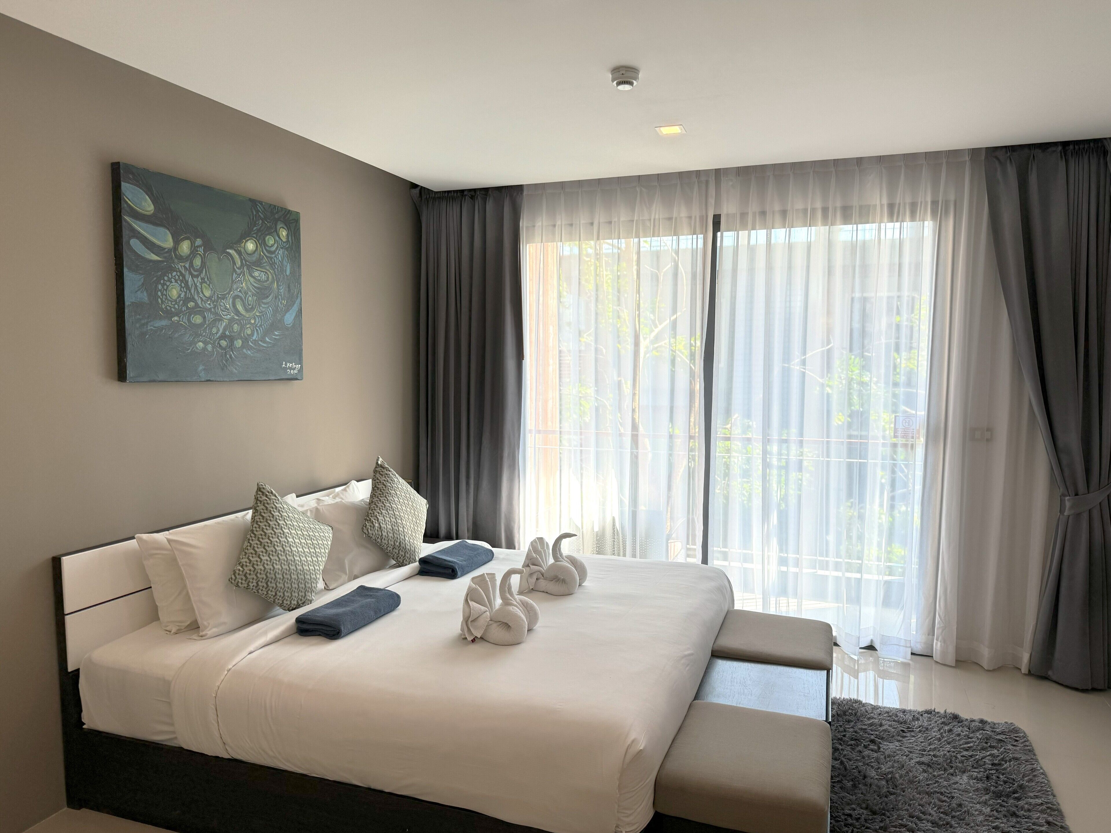 A modern bedroom with a large bed, a painting on the wall, and sheer curtains.