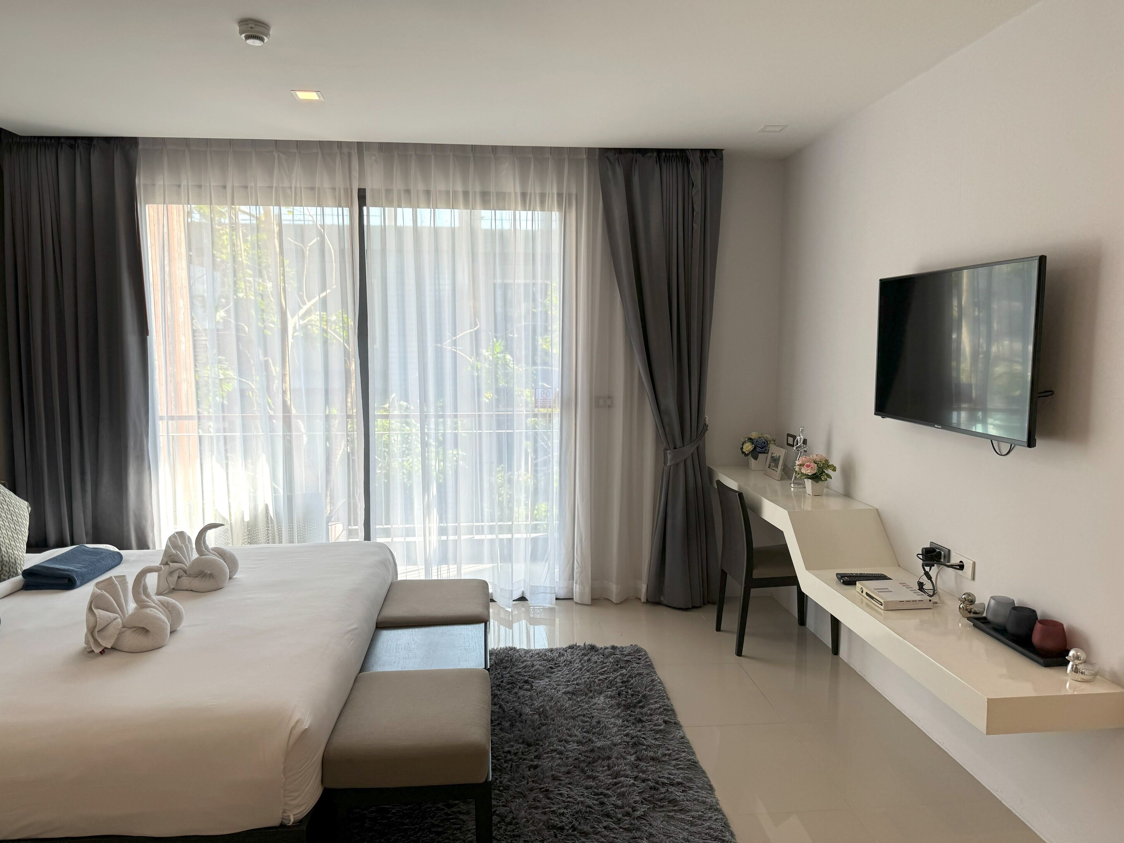 Habitación de hotel moderna con una cama grande, un escritorio con silla, televisor de pantalla plana y vista a árboles por la ventana.