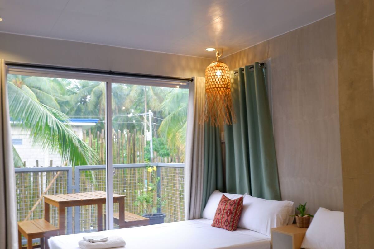A hotel room with two beds, a balcony, and a view of palm trees.
