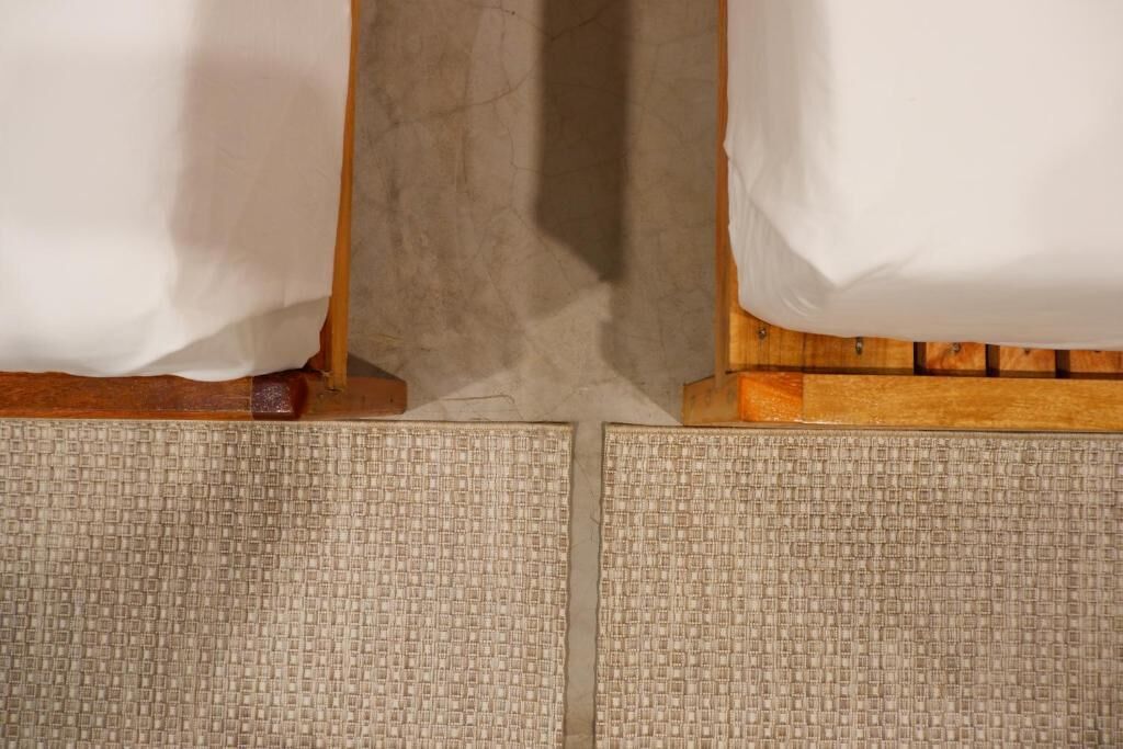 A room with a wooden floor, a visible gap between the bed and the wall, and a textured rug.