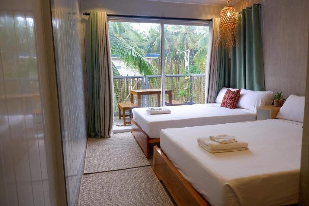 Habitación de hotel con dos camas, un balcón y vistas a palmeras, y una lámpara colgante.