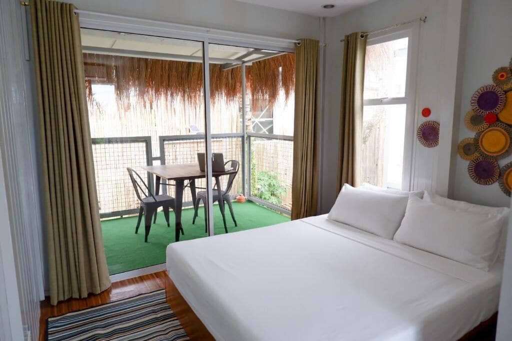 A hotel room with a bed, a dining table with chairs, a balcony with a view, and a green carpet.