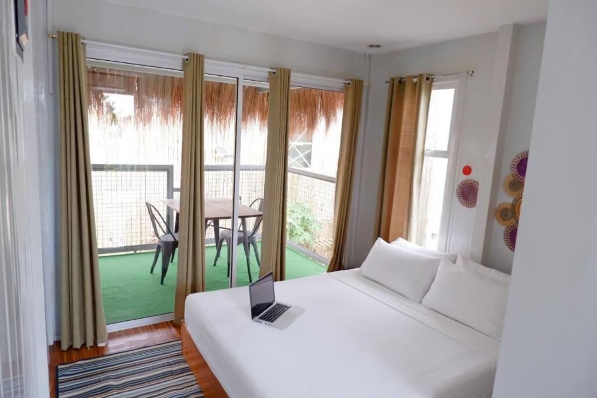 A hotel room with a bed, a laptop on the bed, a balcony with a table and chairs, and a view of the outside.