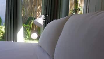 Una cama con sábanas blancas, una lámpara de noche y vistas a una cerca de bambú a través de una ventana.