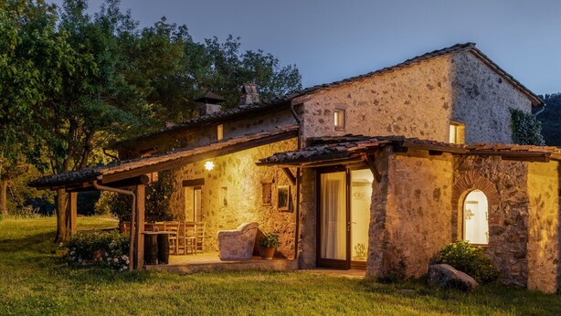 Una casa de pedra rústica amb un pati, seients a l'aire lliure i una entrada ben il·luminada.