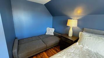 Une pièce avec un canapé gris, un lit blanc, une table de chevet avec une lampe et un mur bleu.