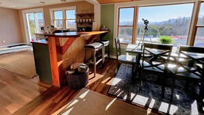 A spacious kitchen with wooden beams, a bar area, and large windows offering a mountain view. - 64J Stunning sunsets, just 20 mins to Bretton Woods. Hot Tub, Foosball, AC, dog friendly! (Whitefield)