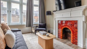 Una sala de estar con chimenea, un sofá, una mesita de centro y un televisor sobre la chimenea.