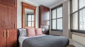 Un dormitorio con una cama grande, un armario de madera, un espejo y una ventana con persianas.