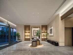 A modern lobby with a marble floor, a central seating area, and a reception desk.