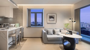 A modern apartment with a kitchen, a dining area, a living room with a sofa and a coffee table, a large window with a city view, and a framed artwork on the wall. - Somerset Pudong Riverside Shanghai (Shanghai)
