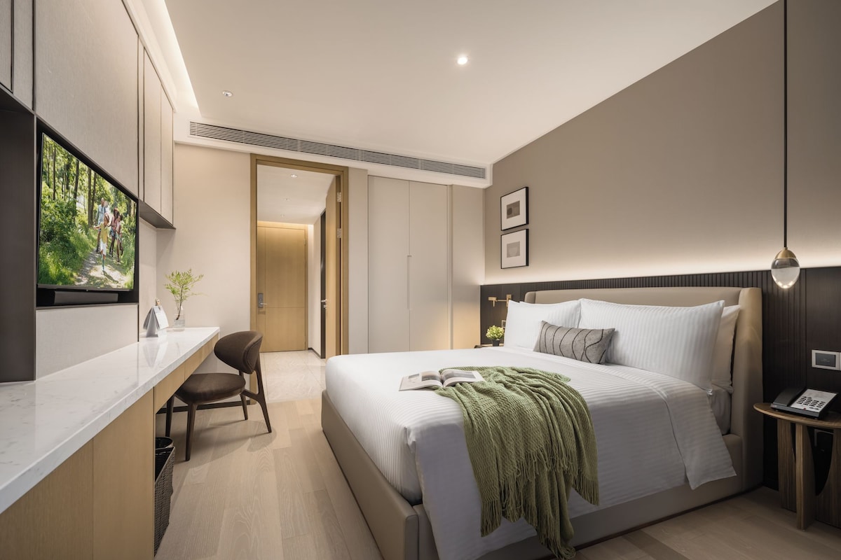 A modern hotel room with a large bed, a desk, and a television.