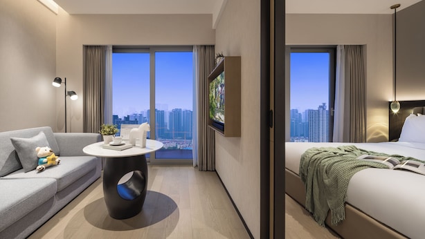 A modern hotel room with a sofa, a round table, a bed, and a large window offering a city view. - Somerset Pudong Riverside Shanghai (Shanghai)