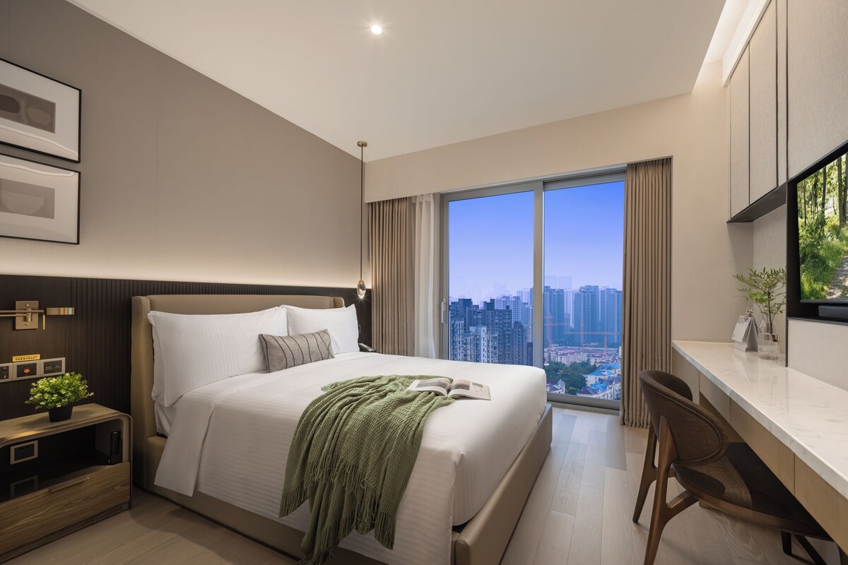 A modern hotel room with a large bed, a desk, and a city view.