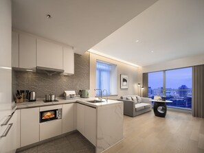 A modern kitchen with a built-in oven, a dining area with a sofa, and a large window offering a city view. - Somerset Pudong Riverside Shanghai (Shanghai)