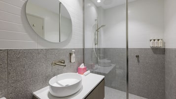 Un baño moderno con un espejo redondo, un lavabo blanco y una zona de ducha con mampara de vidrio.