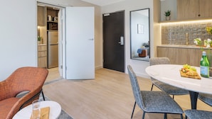 A modern kitchen with a built-in oven, a dining area with a round table and chairs, and a small seating area with a sofa and armchair. - Punthill Maitland (Maitland)
