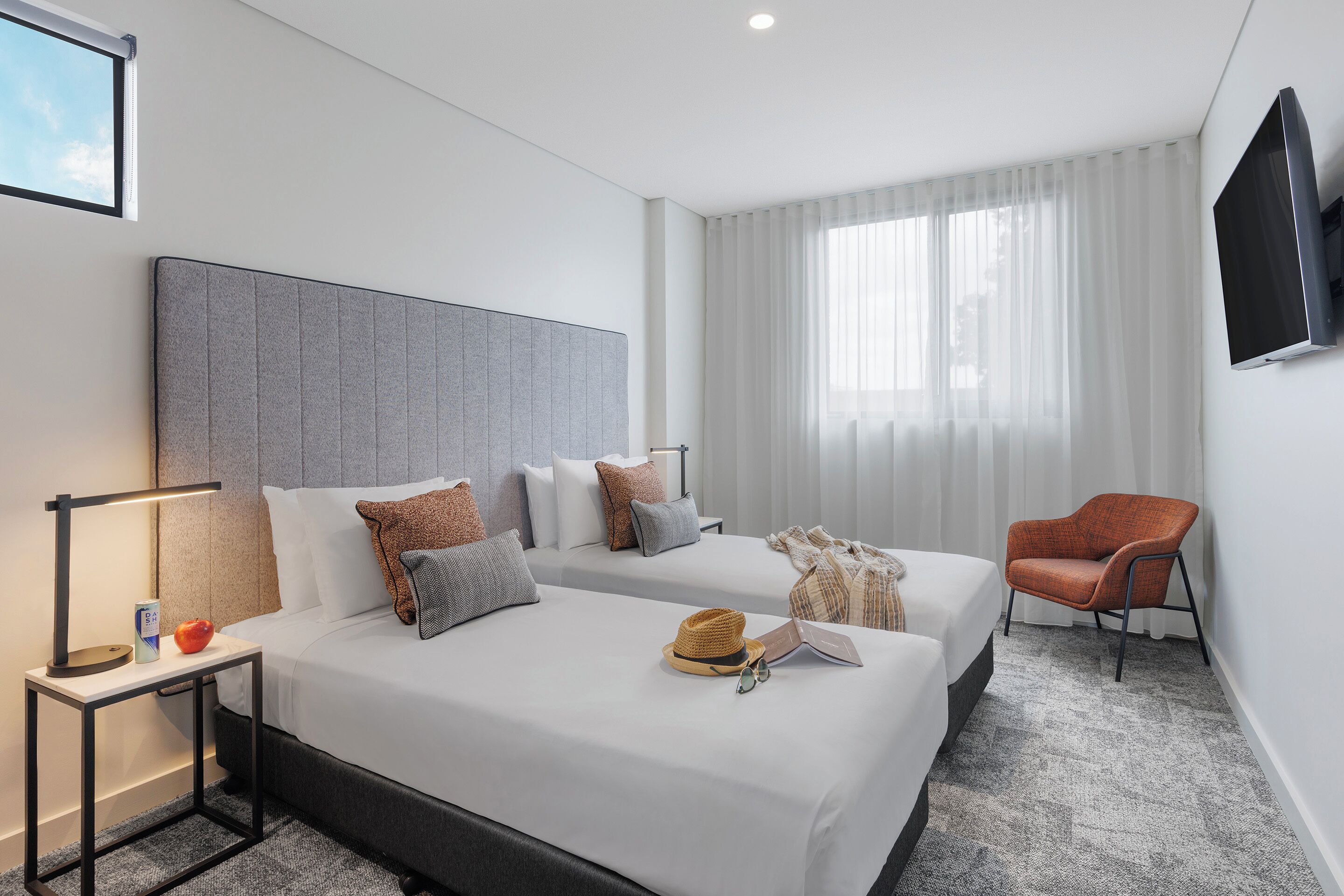 A hotel room with two beds, a TV, a chair, and a window with curtains.