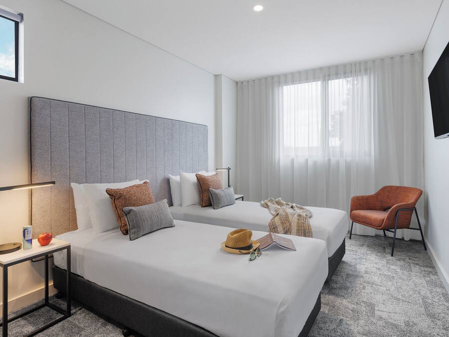 Habitación de hotel con dos camas, un televisor, una silla y una ventana con cortinas.